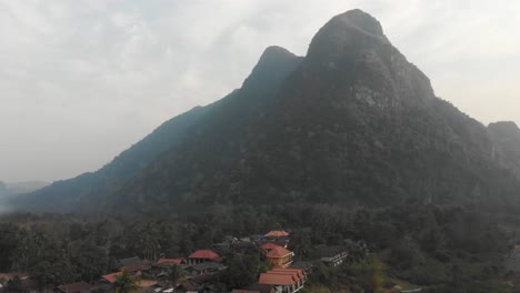 Pequeño-Pueblo-Muang-Ngoy-En-Laos-Con-Una-Gran-Montaña-Al-Fondo,-Aéreo