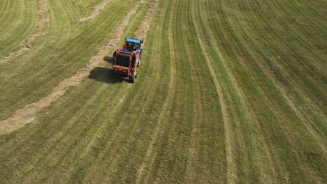 tracking aerial shot of tractor harvesting field, collecting hay to create bales