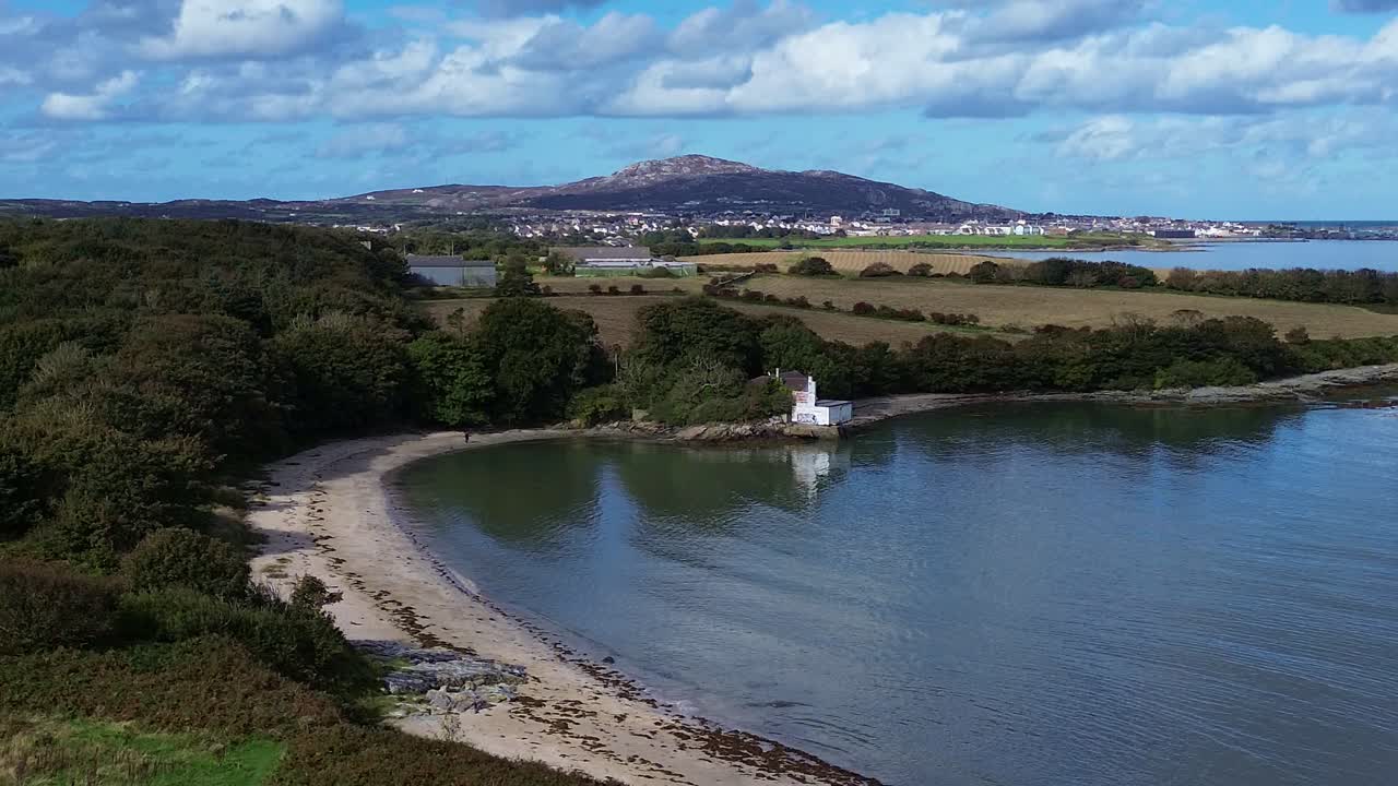 Aerial view establishing Welsh crescent bay under idyllic Holyhead mountain and distant woodland