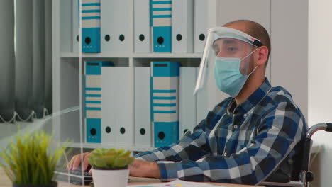 Disabled-businessman-with-face-protection-working-on-computer