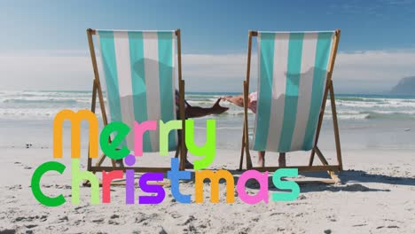 animation of merry christmas over senior biracial couple sunbathing on beach