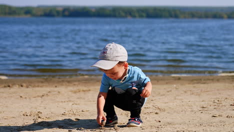 cute baby boy sits at the beach looking for the stones. child heads to the water to throw the pebbles.