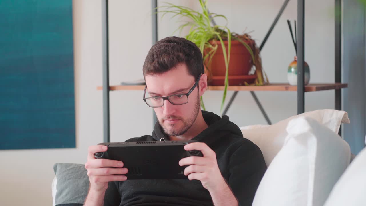 Giovane uomo hipster che gioca ai videogiochi su console portatile.