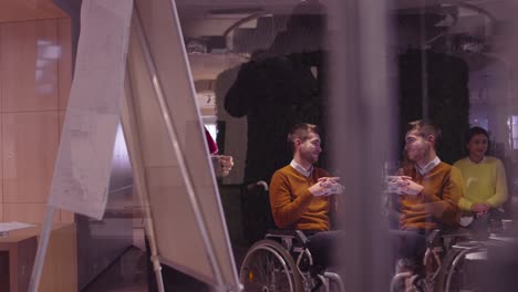 muslim woman in a modern open space coworking office giving a presentation to team. middle eastern arab businesswoman in creative startup office. disabled businessman in a wheelchair on team meeting