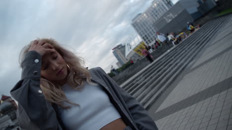 cheerful woman touching hair in modern city buildings street.