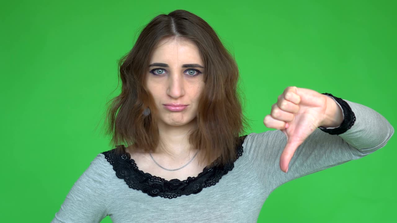 Young woman showing thumb down. Posing against a removable chroma key background.