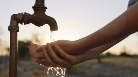 Nahaufnahme-Einer-Frau,-Die-Sich-Bei-Sonnenaufgang-Auf-Ländlichem-Ackerland-Die-Hände-Unter-Leitungswasser-Mit-Frischem-Wasser-Wäscht