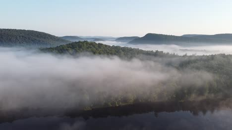 Forest-lake-in-early-morning-with-low-hanging,-misty-clouds-in-remote-mountain-forest