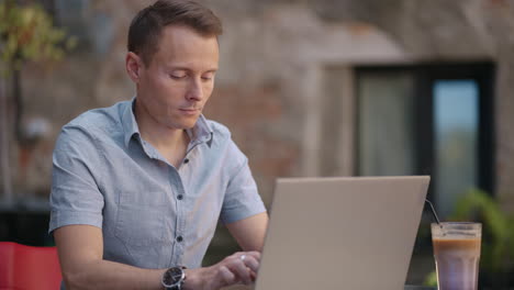 Handsome-freelancer-businessman-in-glasses-diligently-working-on-laptop-in-cafe.-Man-typing-on-keyboard-and-searches-new-job-on-internet-at-coffee-shop.-Business-concept