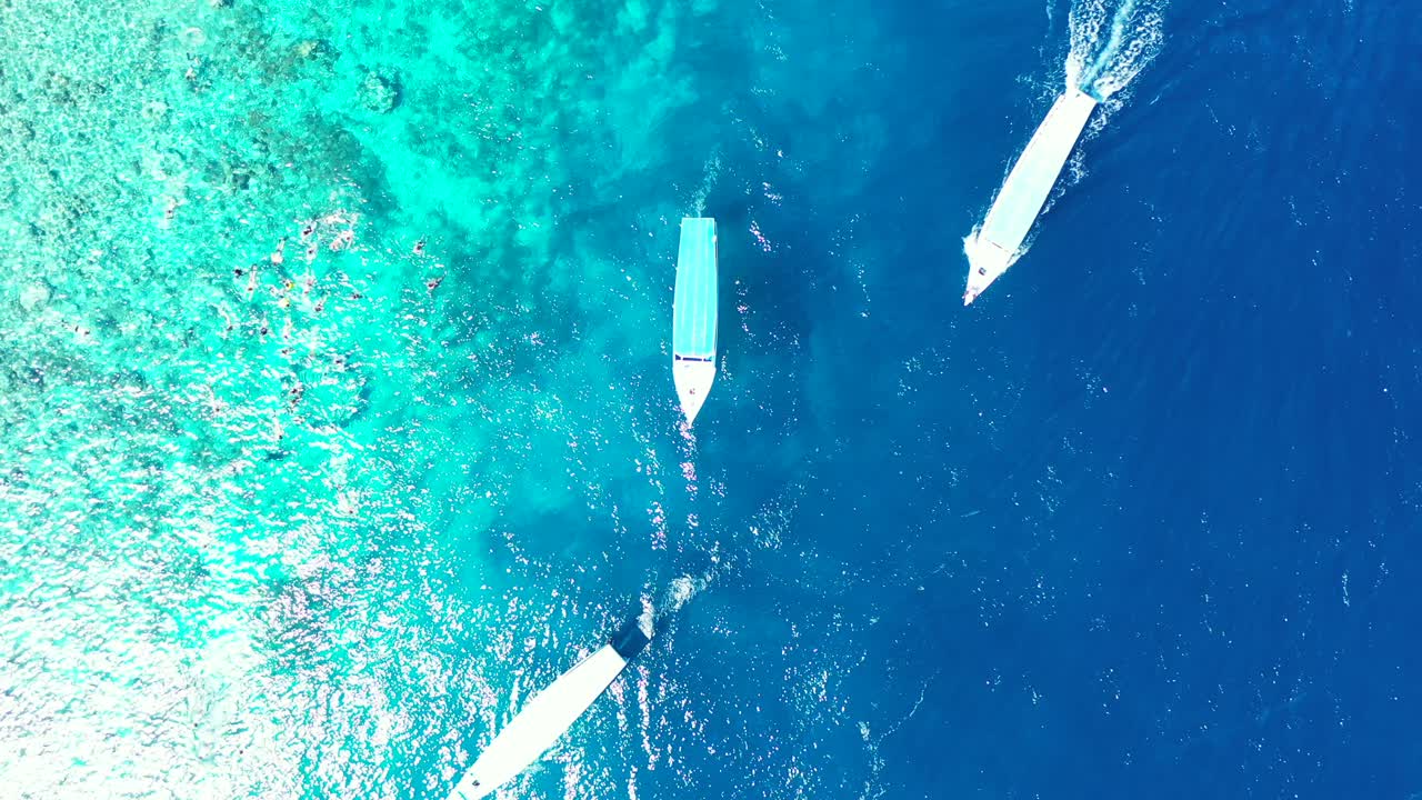 Top view of boats sailing across blue turquoise sea lagoon near shoreline of tropical island, group of people swim, snorkel and dive into sea