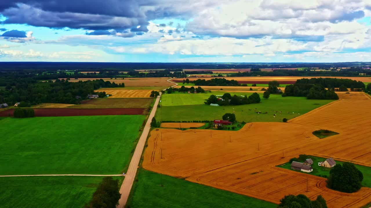 Drone view of farmland landscape with dirt roads and patchy fields under clouds