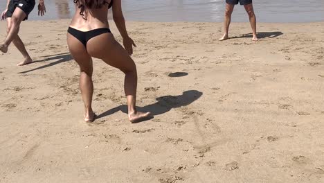 Woman-in-shape-hits-the-ball-with-her-hand-while-playing-on-the-beach-with-friends-in-Lisbon