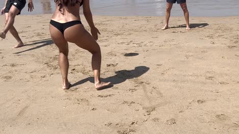 woman in shape hits the ball with her hand while playing on the beach with friends in lisbon