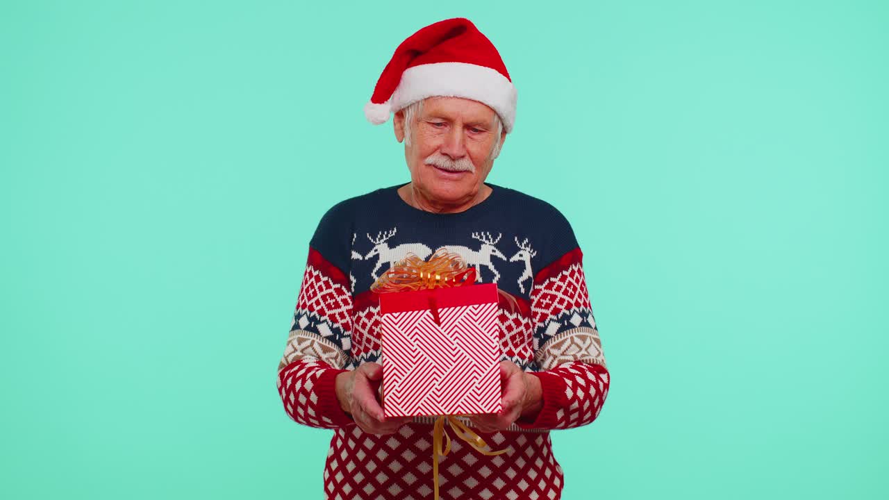 Senior grandfather in new year sweater and hat presenting christmas gift box shopping sale holidays