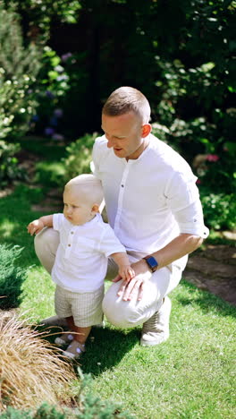 caucasian man sits squatted and his baby son standing leaning on him. father and child in the nature. vertical video.