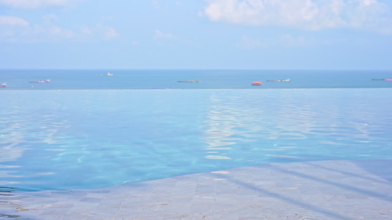 Shimmering calm water of infinity edge swimming pool overlooking the sea with boats on the surface in the background. Tropical island resort vacation destination with azure sea and sky