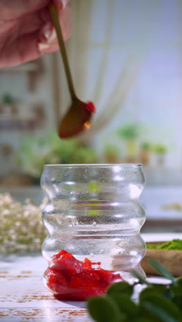 a spoonful of vibrant red strawberry jam hovers above a curvy glass, about to drop into the base for a layered drink. perfect for recipe reels, aesthetic food content, or healthy drink ads.