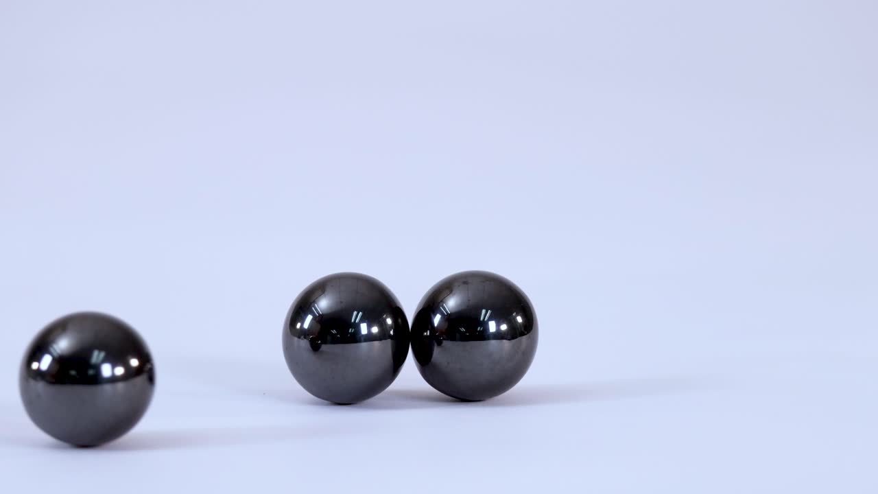 Close-up shot of three metallic magnetic balls rolling together and connecting on a white background