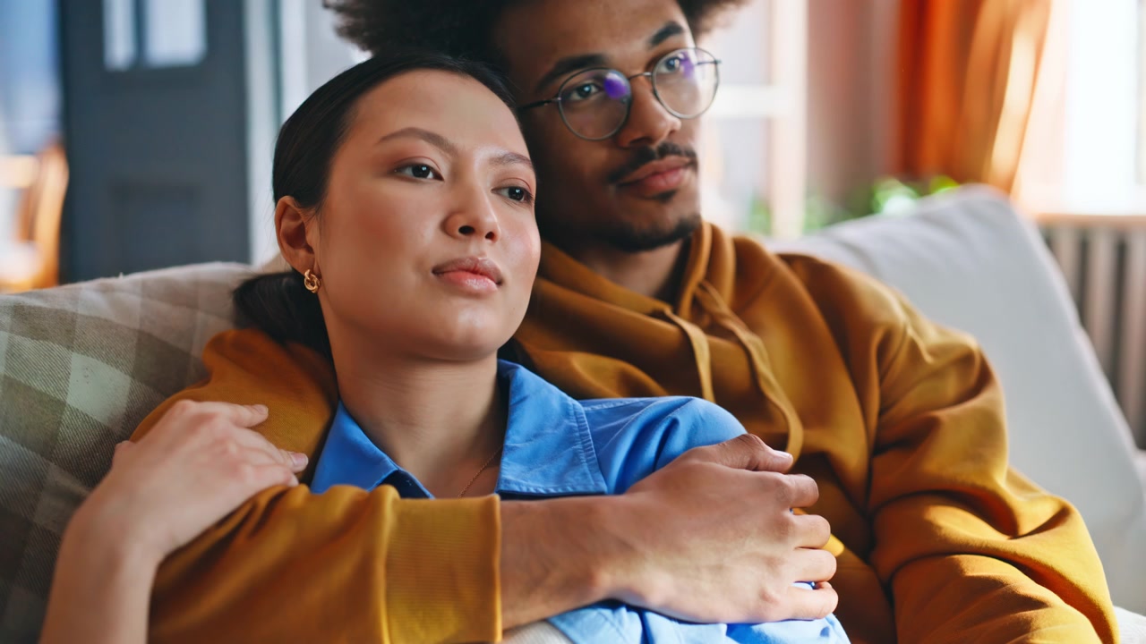 Pareja tomándose de la mano en el sofá de casa. Primer plano de pareja multirracial relajándose
