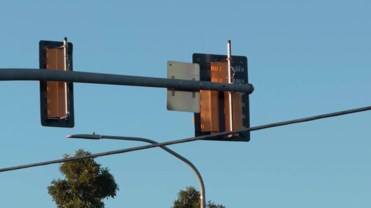 Foto infrastruktur lampu lalu lintas dan lampu jalan yang bersiluet di latar belakang langit senja yang cerah.