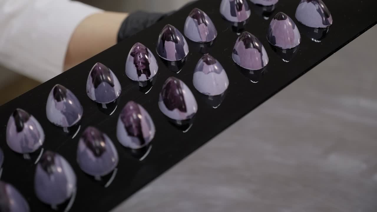 el chef de pastelería sostiene caramelos de color chocolate hechos a mano en un soporte de espejo negro
