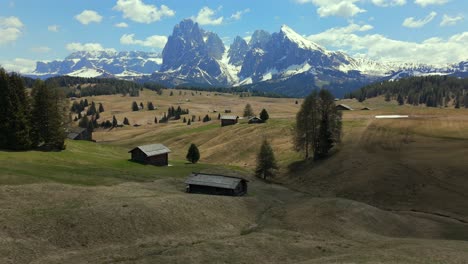 panoramic view of alpe di siusi with traditional wooden huts scattered across the rolling meadows, set against the stunning backdrop of the sassolungo mountain range