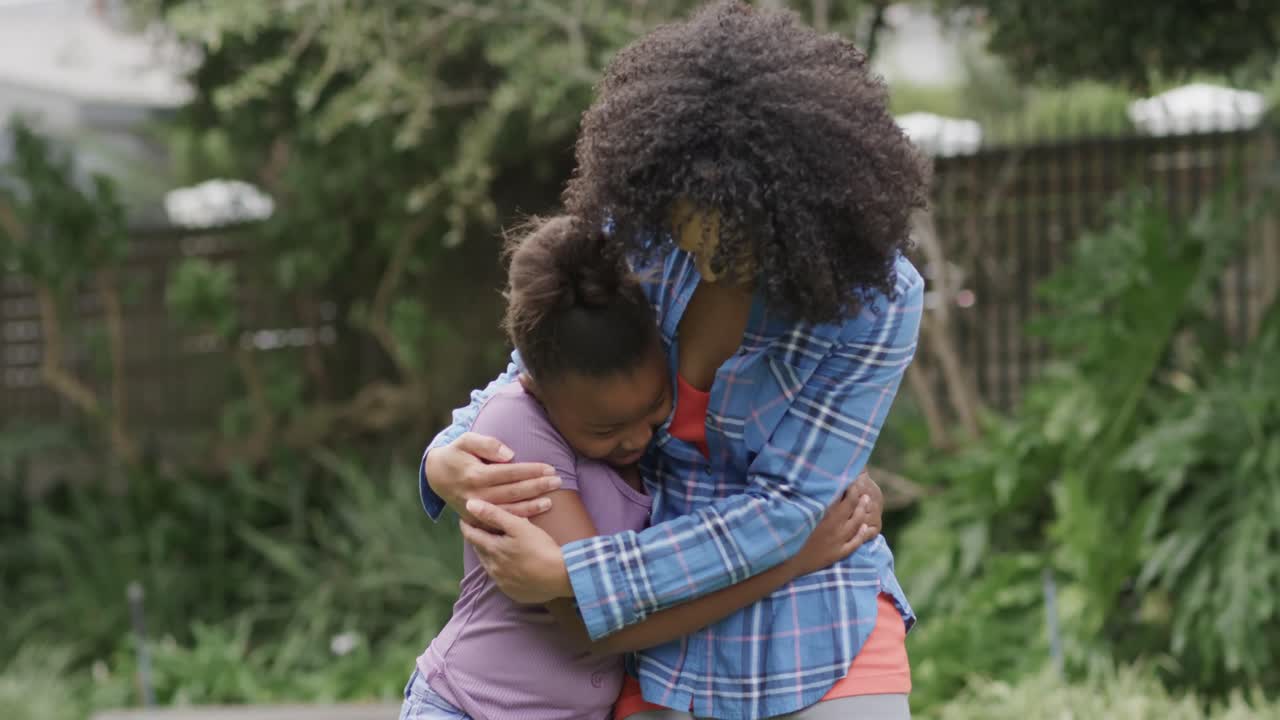 retrato de una feliz madre y hija afroamericanas abrazándose y sonriendo en el jardín, cámara lenta