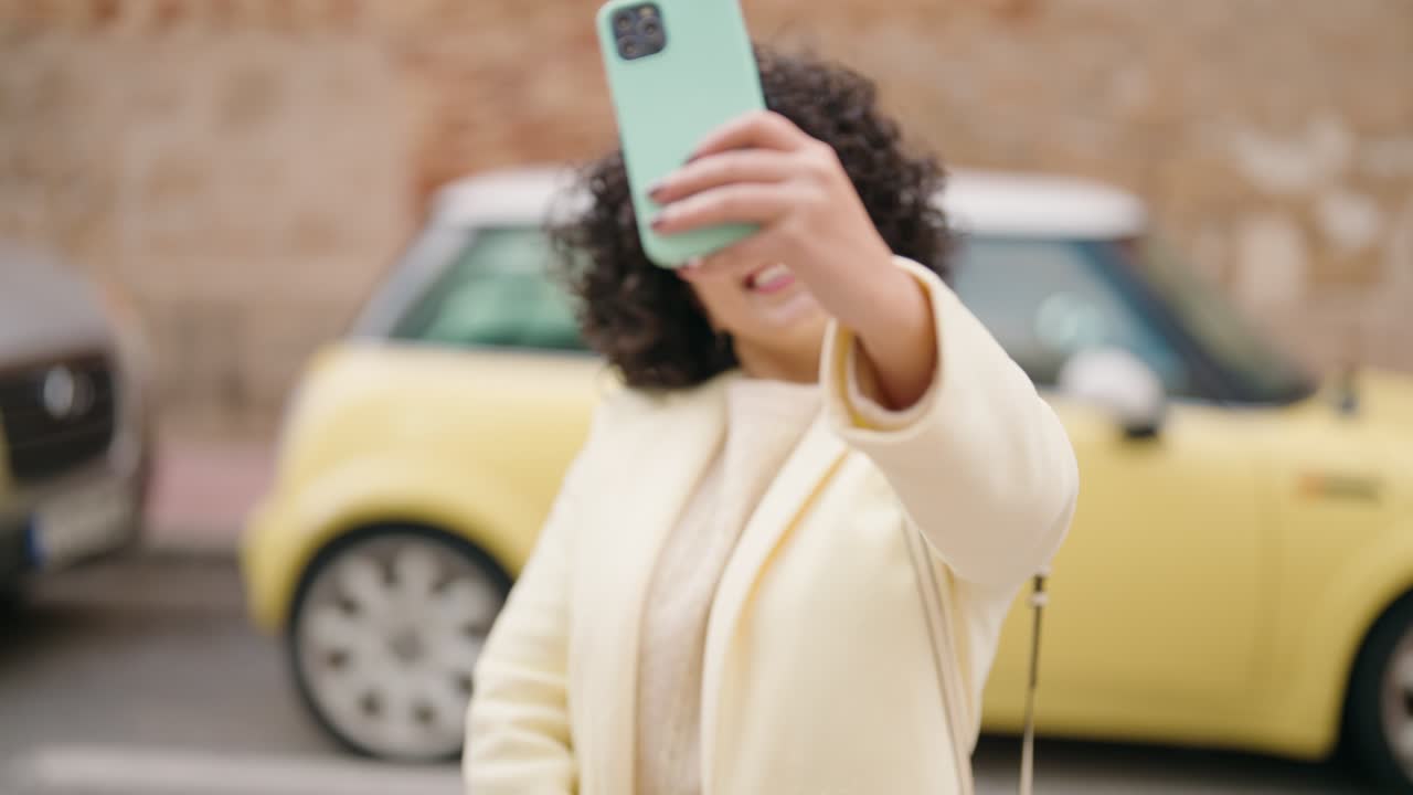 joven sonriendo confiada tomando una selfie con el teléfono inteligente en la calle