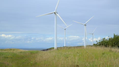 Wind-turbines-spinning-against-cloudy-sky-with-rise-up-reveal-of-coastline