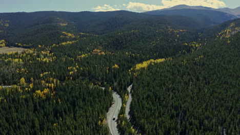 Aerial-view-panning-down-to-truck-on-mountain-forest-highway-in-fall,-4K