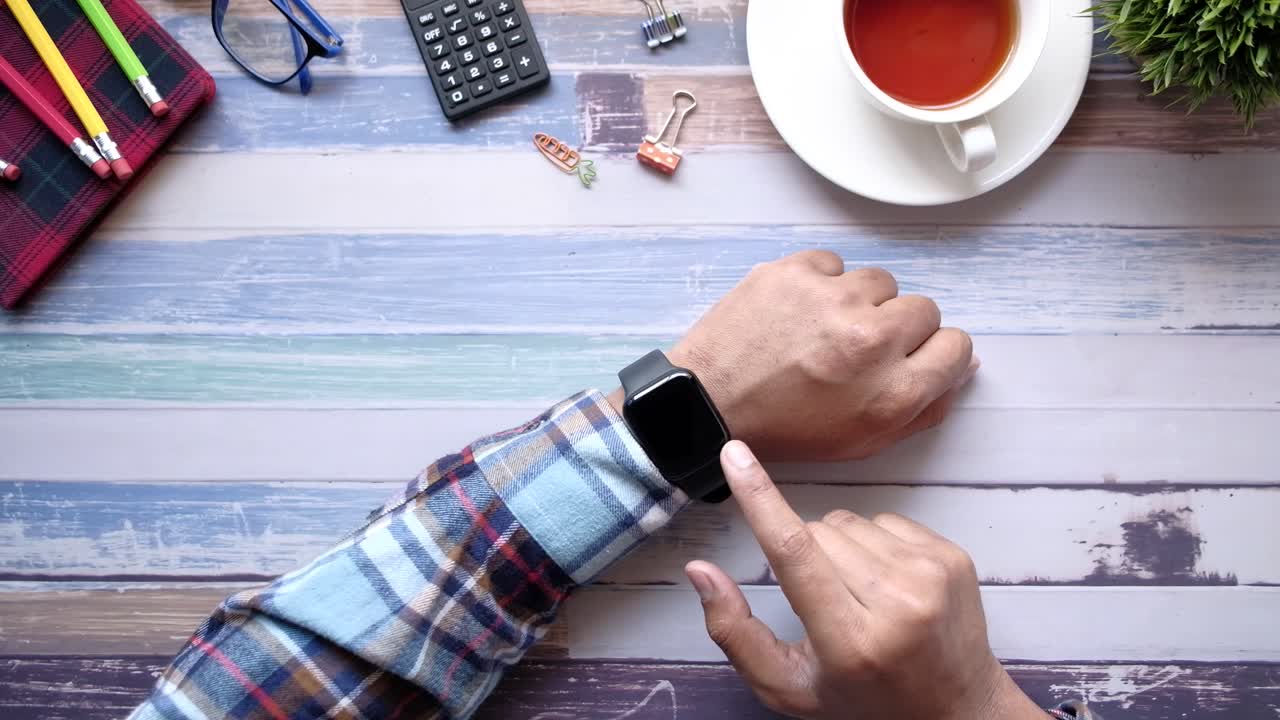 Person using a smartwatch on a wooden desk