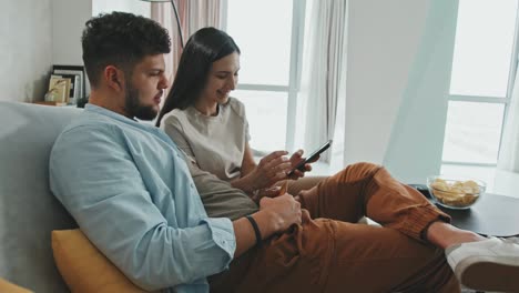 pareja sentada en el sofá de un apartamento, hablando mientras usa smartphones