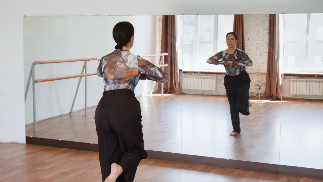 Woman practicing dance in a studio with a mirror reflection