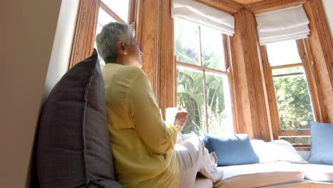 Happy-senior-biracial-woman-sitting-on-couch-and-drinking-tea-at-home,-slow-motion