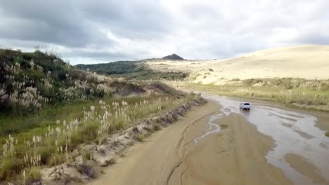 4WD-vehicle-driving-along-Te-Paki-Stream-by-great-sand-dunes-near-Cape-Reinga-in-New-Zealand