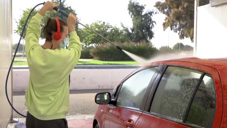 woman cleaning car roof with pressure hose while listening to music with mask on