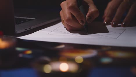 close up of woman using laptop to draw astrology lagna or birth chart on candlelit table 2