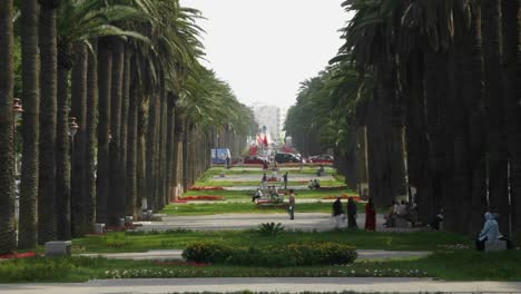 A-time-lapse-of-vehicles-and-pedestrians-passing-through-a-courtyard-surrounded-by-palm-trees-