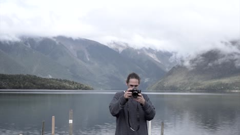 Man taking photos by a lake with mountains