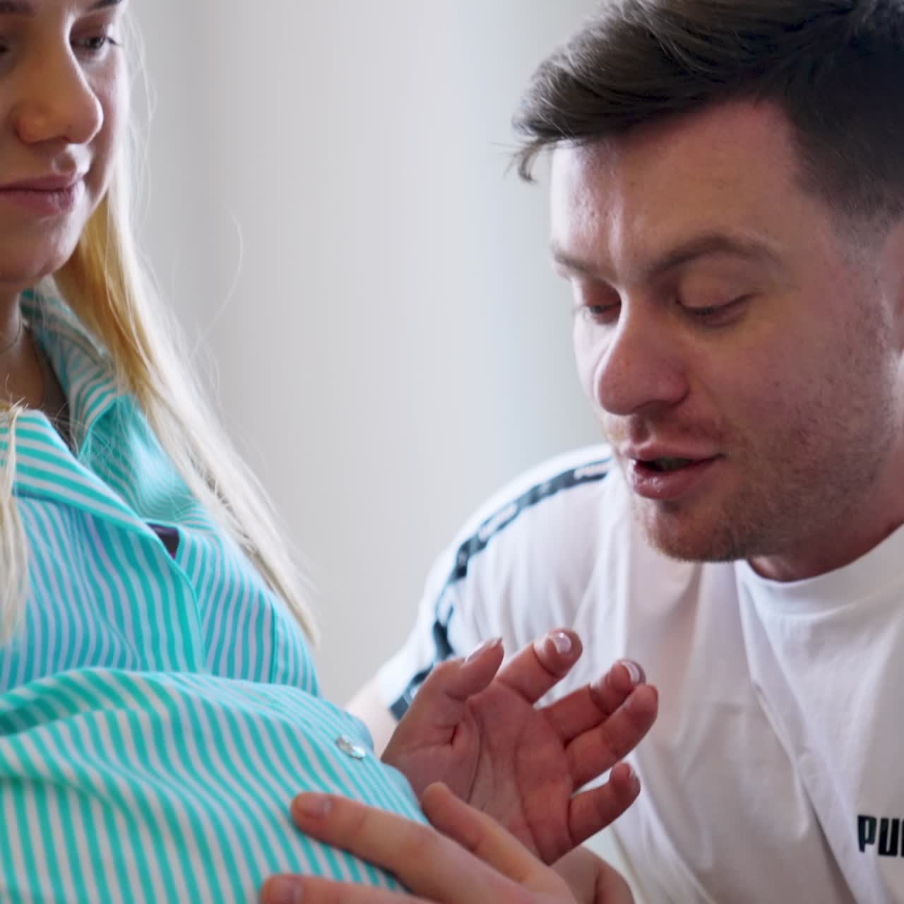 Loving father listens to baby in wife's belly and kisses it. Happy daddy talking to his future child. Low angle view