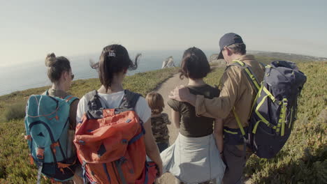 Back-view-of-parents-and-children-walking-along-path-towards-the-sea