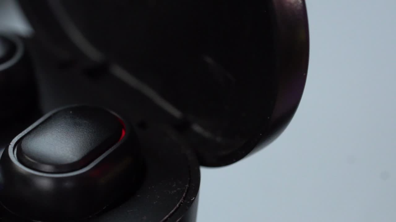 Macro close up of wireless earbuds inside black charging case with digital display, studio shot