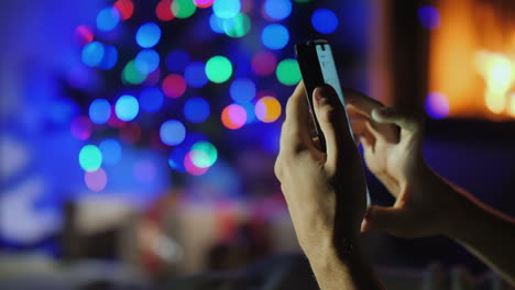 Hände-Mit-Smartphone-Auf-Verschwommenen-Lichtern-Von-Weihnachtsbaum-Und-Kamingeschenkbestellung