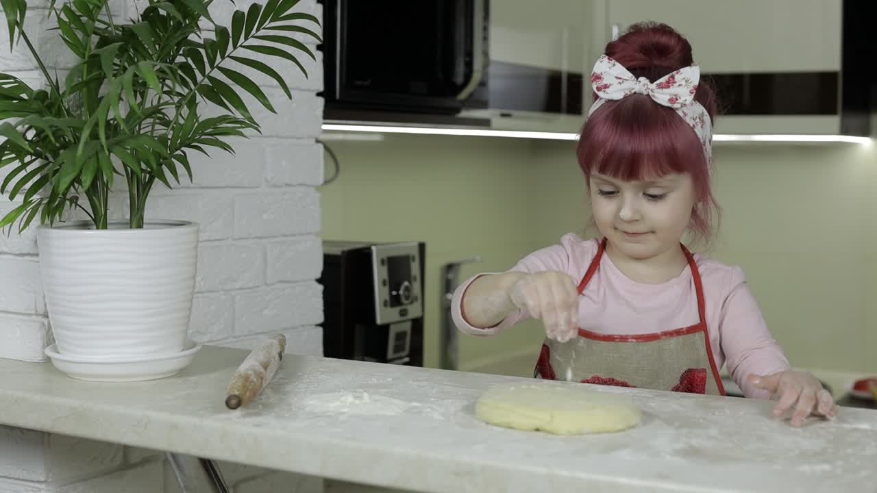 Cooking pizza. Little child in apron sprinkle the dough with flour in kitchen