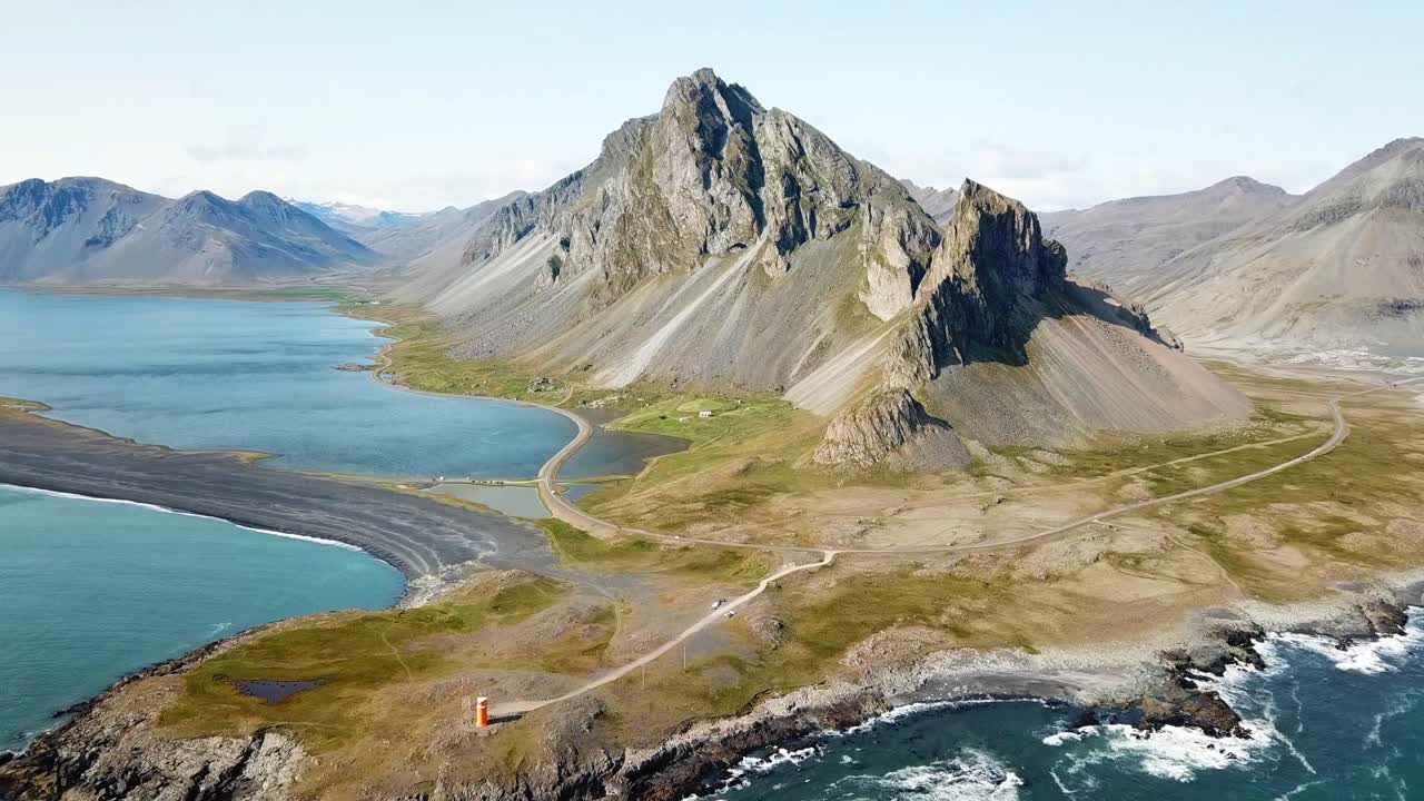 Breathtaking view of Hvalnes in Iceland featuring towering coastal mountains, crystal-clear waters, winding roads, and vibrant green terrain. A perfect representation of Iceland’s natural beauty