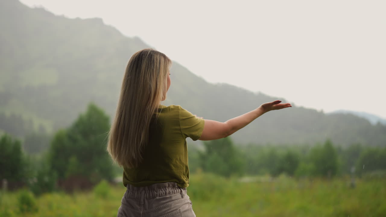 긴 머리카락을 가진 웃는 여인이 따뜻한 여름 비를 즐기고 있습니다.