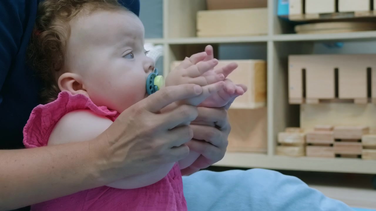 Close-up of an adult holding a baby girl's hands together