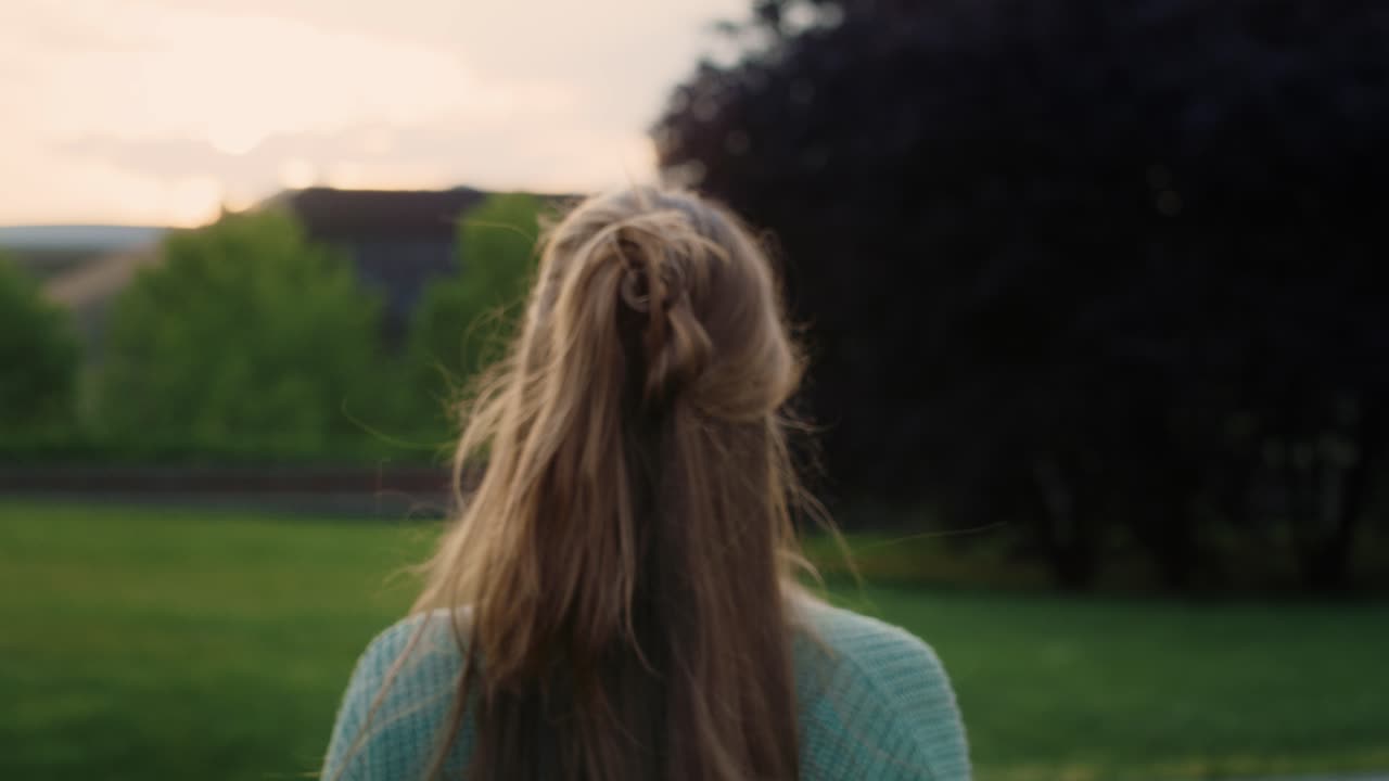 백인 젊은 여성이 공원을 가로질러 걸어서 카메라를 향하고 있습니다.