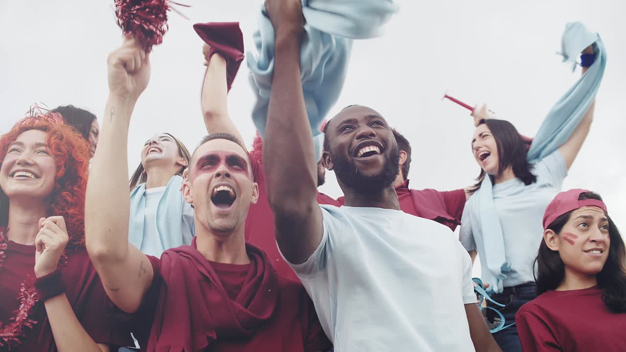 Energetic sport fans supporting their team in the football stadium. Multiracial group of friend enjoying sport soccer event