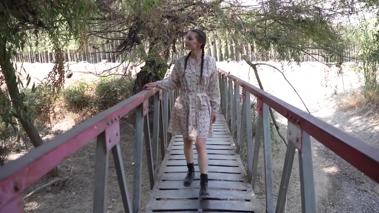 Una giovane ragazza in piedi su un ponte rustico, abbracciata dalla natura lussureggiante tutt'intorno a lei.